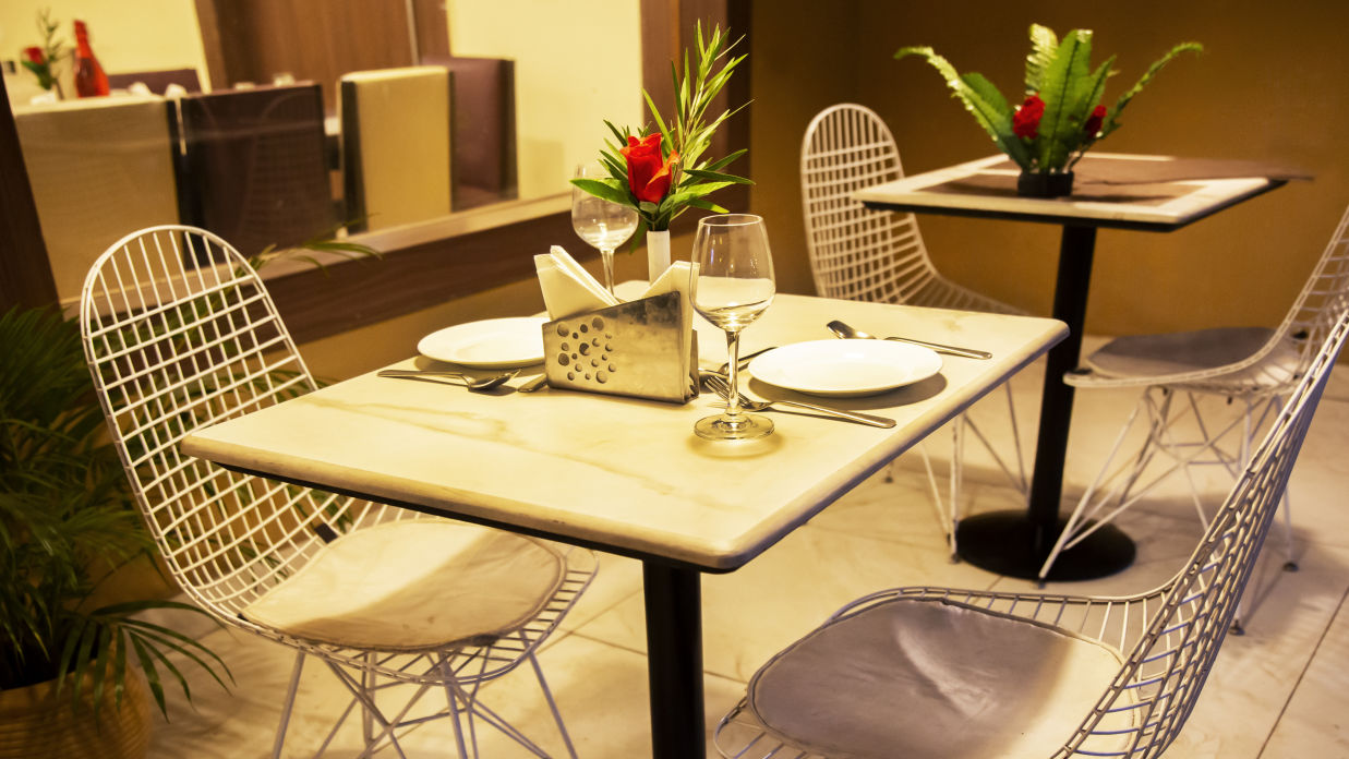 Wine and flower vase kept on table with white chairs arranged for two people