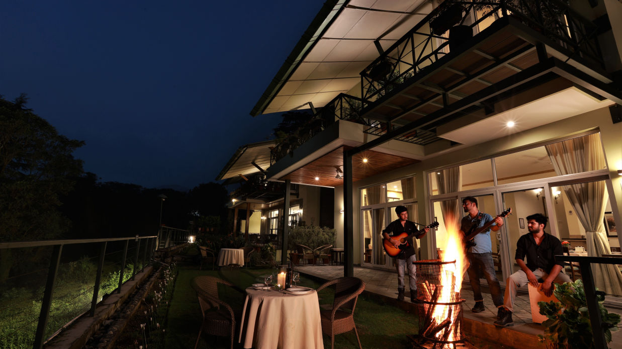 A bonfire with two people playing guitars under the night sky in front of villas at Lamrin Norwood Green, Palampur