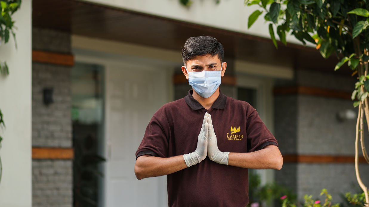 A staff standing with joined hands welcoming guests at a hotel while wearing a mask and gloves - Lamrin Norwood Green, Palampur