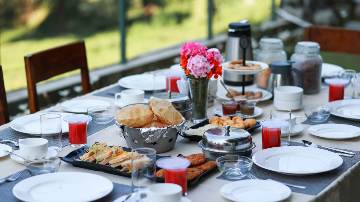 A breakfast table decorated with delicious food and clean white plates with green garden in the background - Lamrin Norwood Green, Palampur