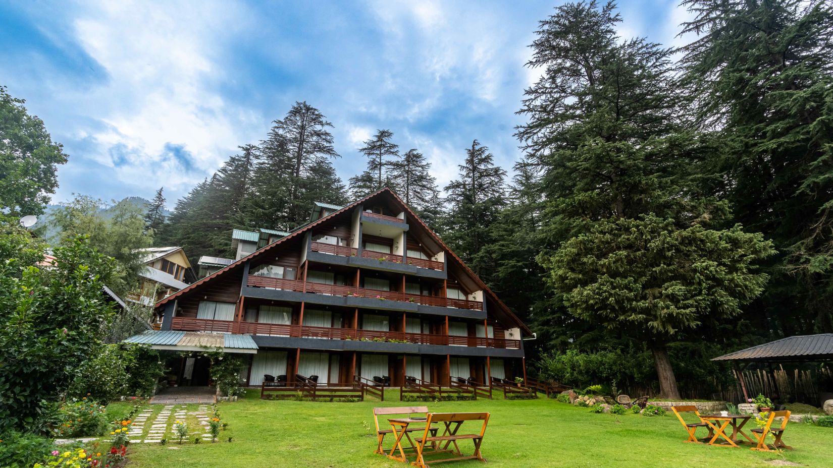 Facade of Bedzzz Xclusiv Baikunth, Manali with sitting area in front of it and surrounded by trees