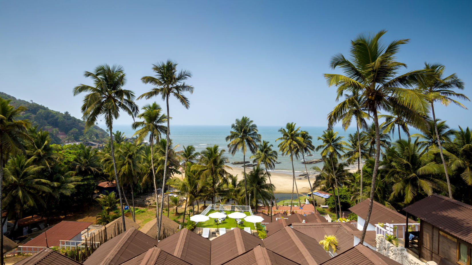 an upper angle view of the sea from cottages at a resort with coconut trees swaying, and shot during the day - Stone Wood Hotels & Resorts