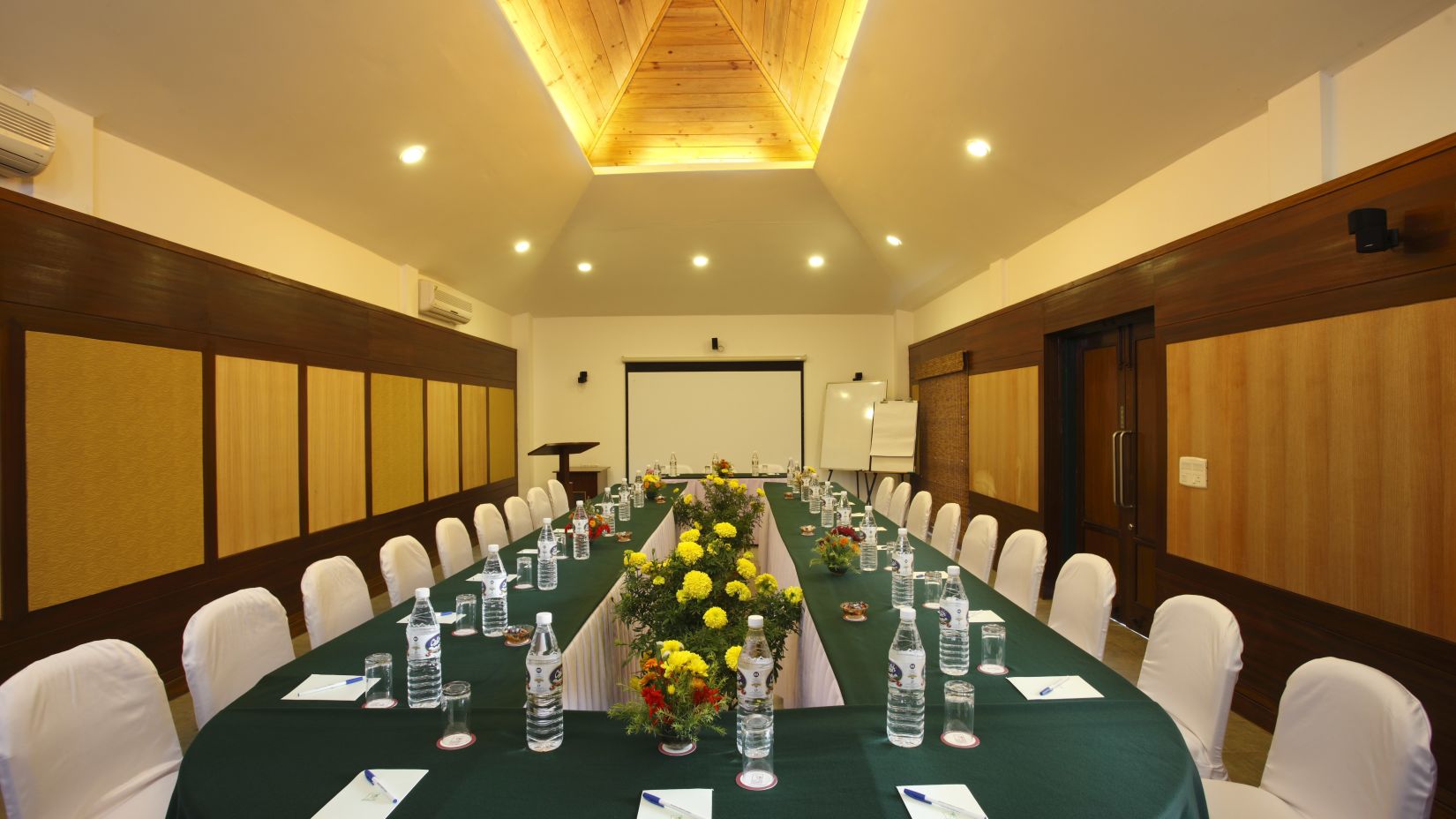 a meeting room with a large table surrounded with chairs and a projector screen on the other end of the hall - Baikunth Resort, Kasauli