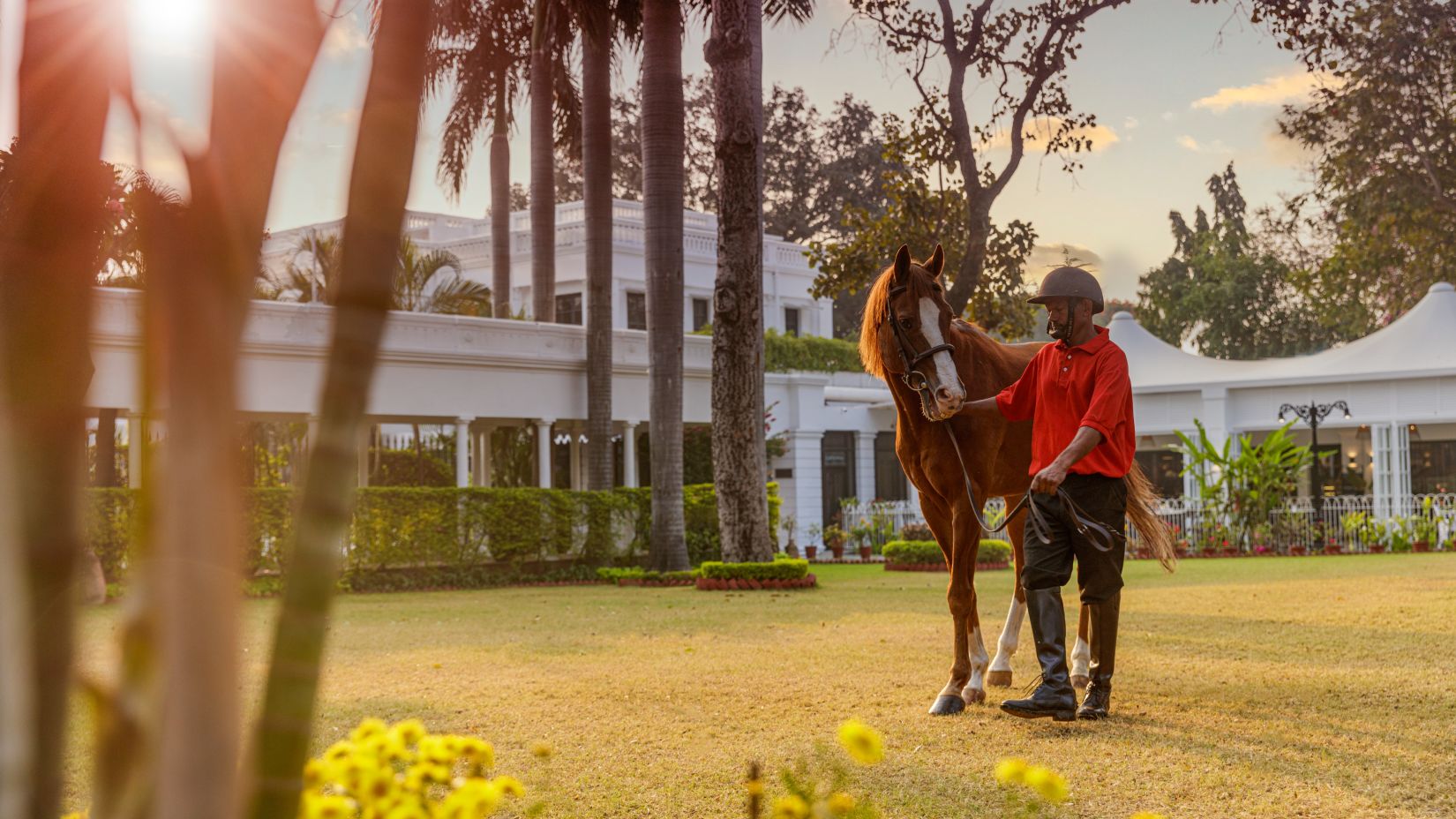 A jocket next to a horse with a building in the background