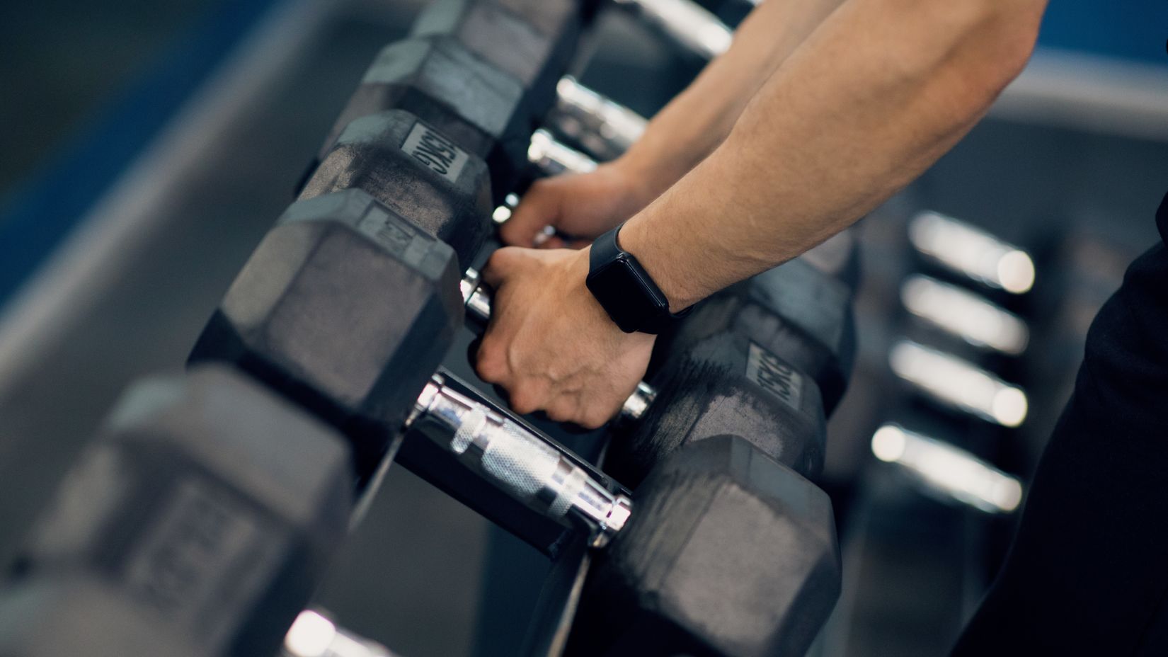 a close up shot of a man picking up dumbbells from a tray of dumbbells - La Maison Hotel, Doha