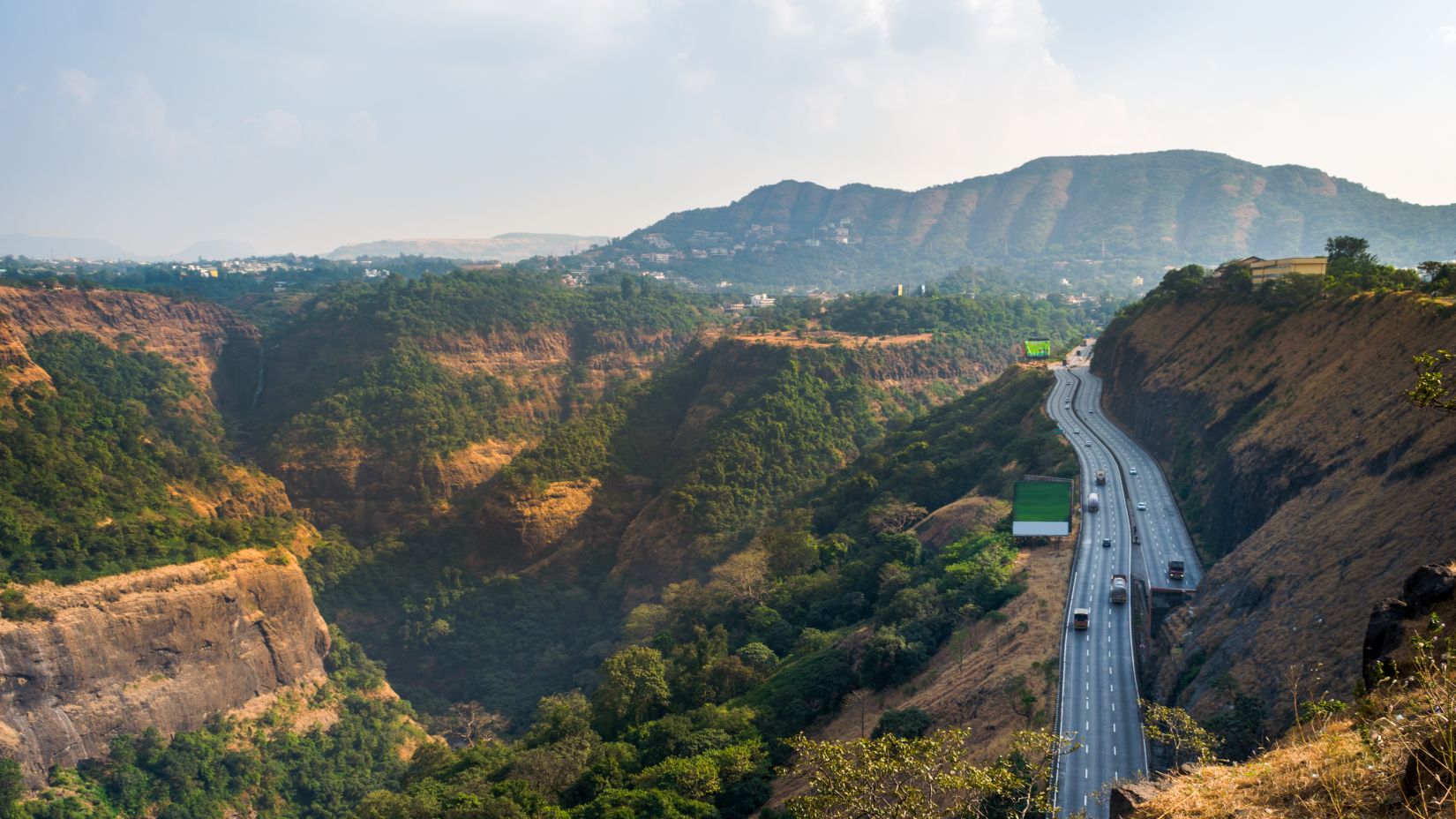 Vehicles on the hill road under clear blue sky of Lonavala showcasing lush greenery