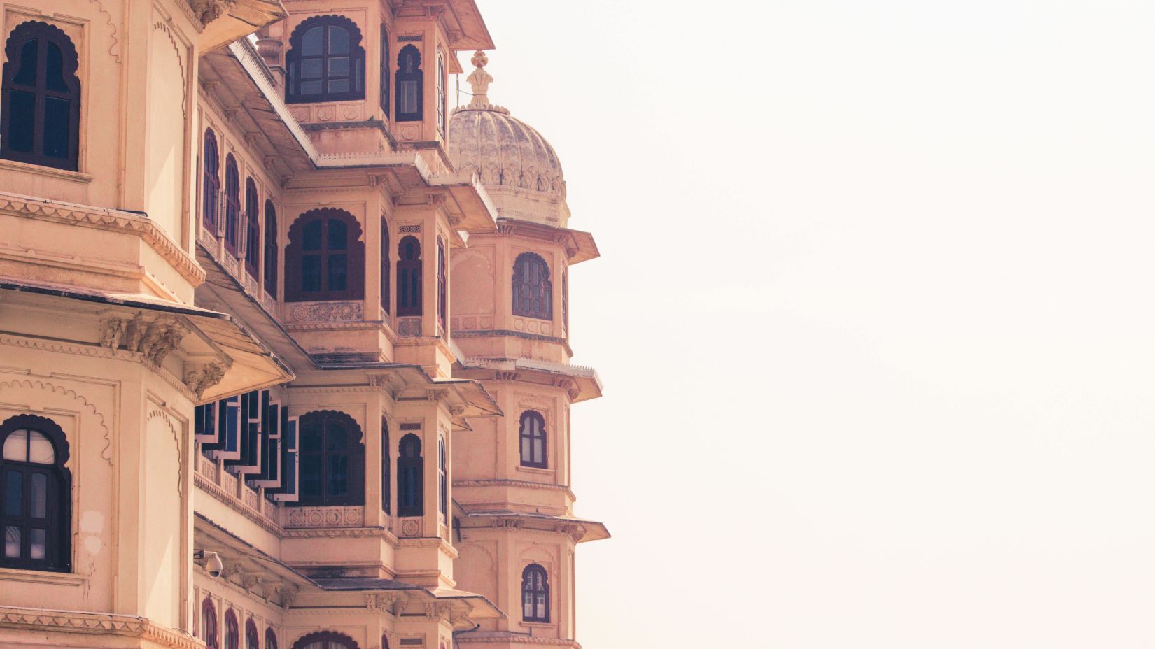 the delicate colours of an Udaipur palace facade set against a light sky, showcasing the city's graceful domes and curves