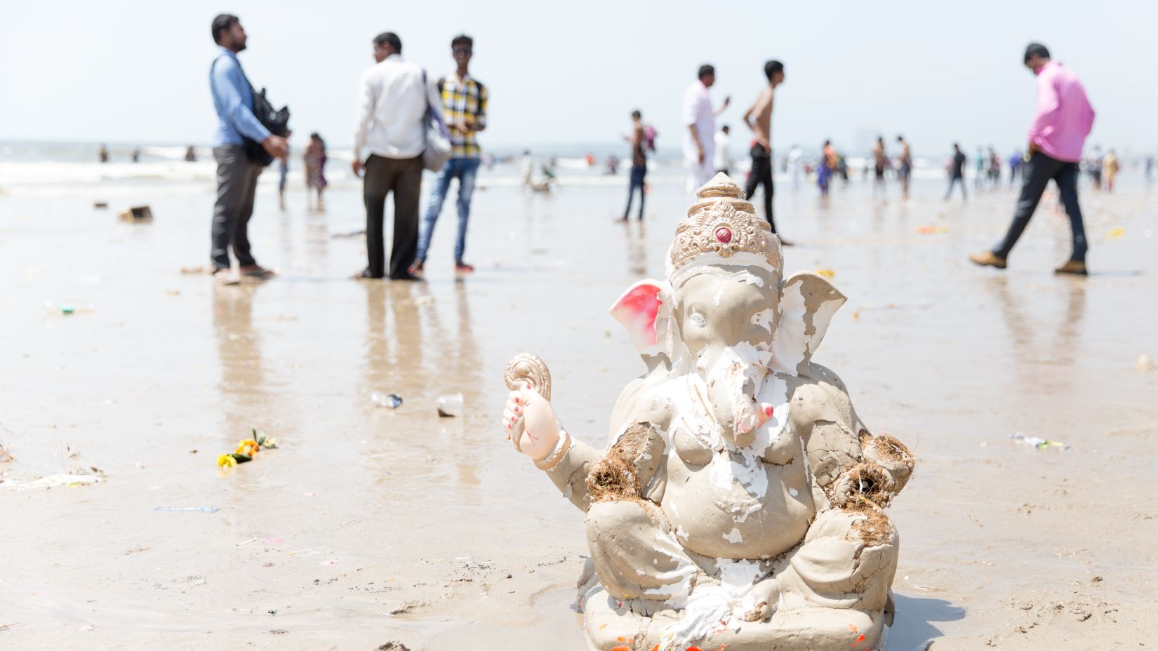 a white idol of lord Ganesha at Juhu beach with people walking around