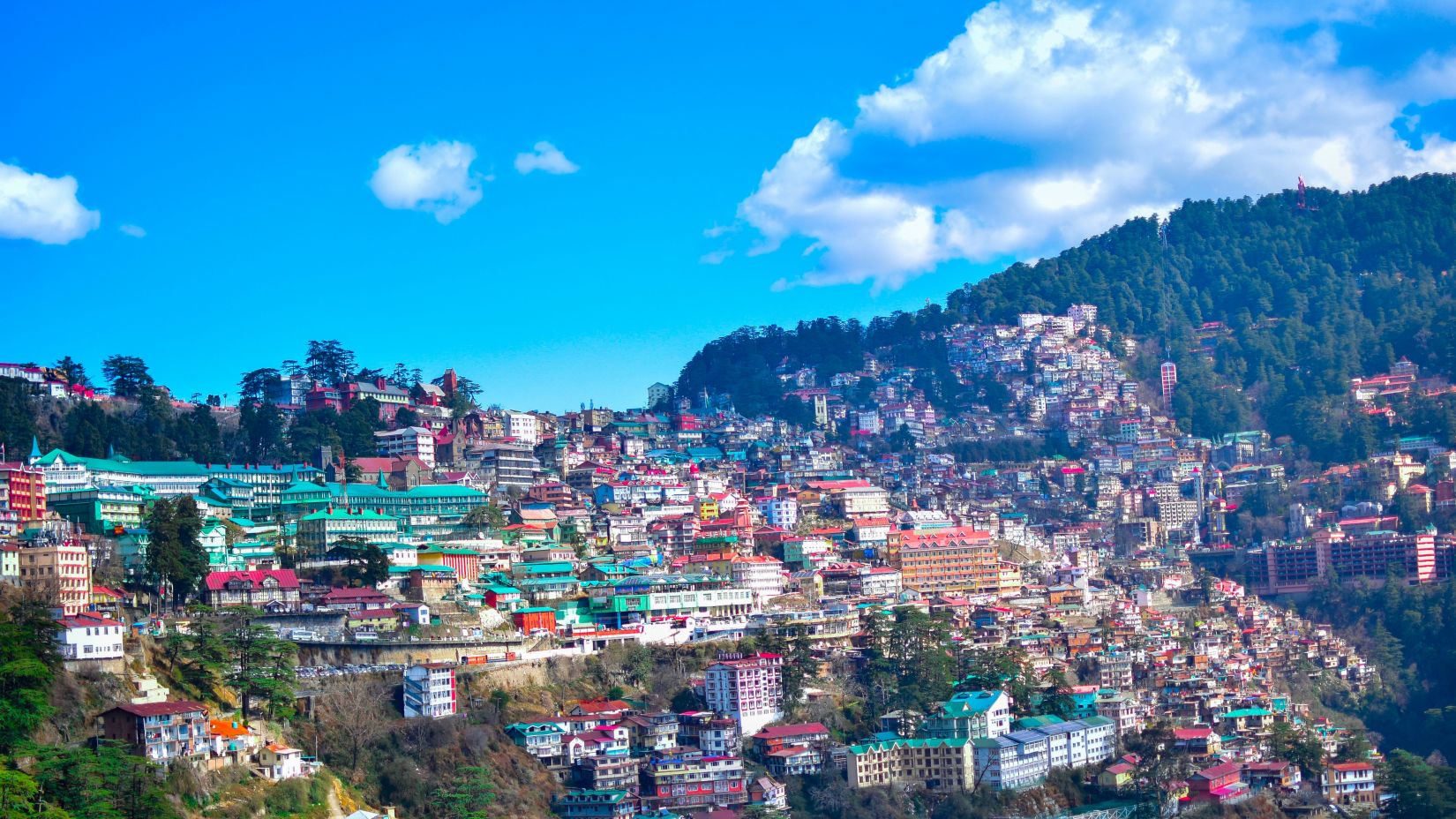 an overview of the town of Shimla with building on the hills and blue sky in the background