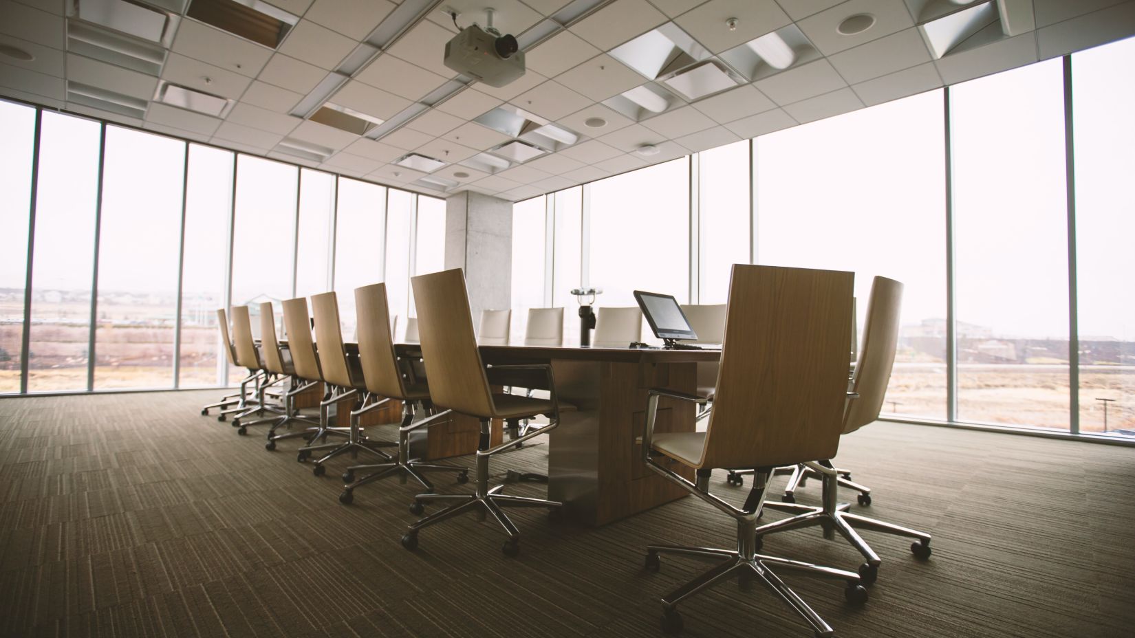 A rectangle shaped table with chairs under with floor to ceiling windows