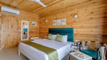 A bedroom with a white ceiling fan, AC unit, wooden walls, a teal headboard, and white bedding with a green accent Aralea Beach Resort by Stone Wood, Morjim