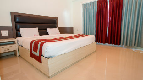 A double bed with side tables and headboard with red and blue curtains on the windows inside one of the Rooms - Hotel Shompen