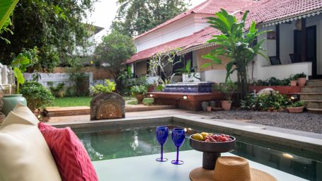 L shaped pool side with two blue wine glasses and surrounded by greenery @ Lamrin Ucassaim Hotel, Goa