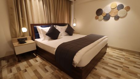 Side angle view of cozy view with bedside table and lamps illuminating the Deluxe King  - Mastiff Hotel, Dhanbad 