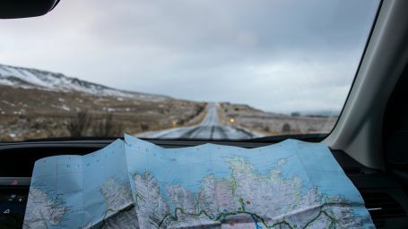 an image of a map kept on the dashboard of a car with a road in the background