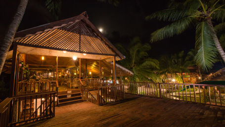 exterior of Venom Bar at night surrounded by palm and coconut trees and decorated by soft yellow lights - Symphony Palms Beach Resort And Spa