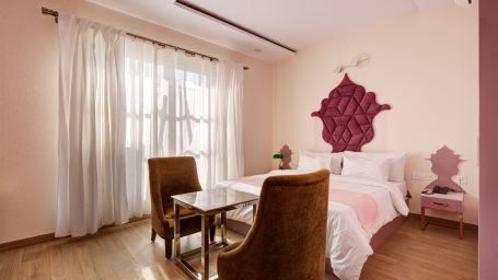 Pink themed Super Deluxe Room with king size bed, chairs and white curtains - The White Moon