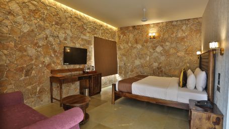 A room with a well made bed, TV, a sofa chair and a mirror - Vikrama Sarovar Portico, Pavagadh