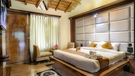 A room furnished with an elegantly adorned bed, two cosy sofa chairs, a coffee table, a carpet and a TV - Vinsober Monal, Nainital