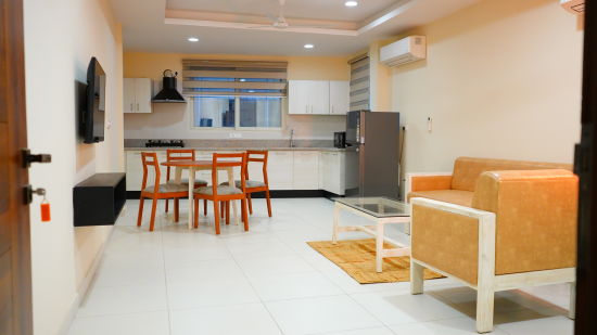 A spacious hall features a sofa, dining table and chairs, a TV and a kitchen - A M Suites