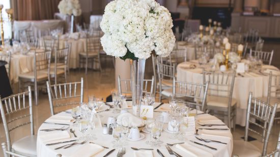 an overview of a banquet hall with round table having cutlery and a vase