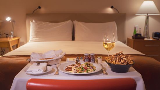 Many items on a table that was served as room service with a double bed in the background