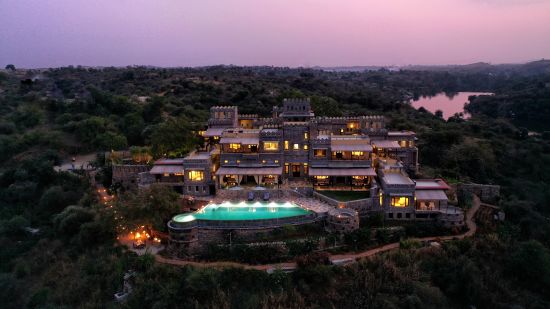 Aerial view of chunda palace with swimming pool and trees covering and evening sky in the background - Chunda Hotels