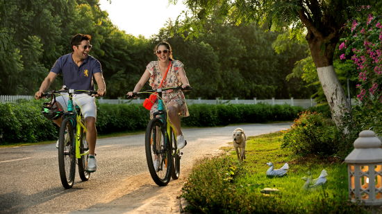 a couple cycling on a stone pathway next to nature and trees with the sun shining from behind them at this Romantic Getaways Delhi - Heritage Village Resort & Spa, Manesar