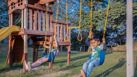 children playing on swings with trees in the background - Karma Lakelands