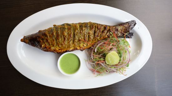 A grilled fish served with a side of salad and green sauce on an oval white plate, offering a culinary delight-Lotus Eco Beach Resort, Konark.