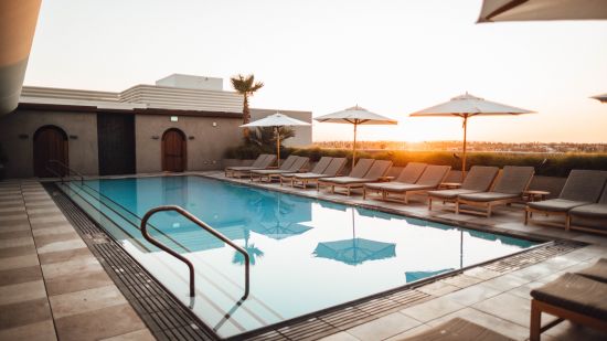 A swimming pool with loungers next to it and the sun setting in the background