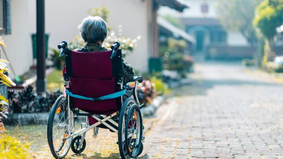 An old person sitting in a wheelchair looking into the distance 