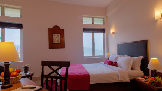 a bed with red duvets and a work desk sitting on one side of one of the rooms