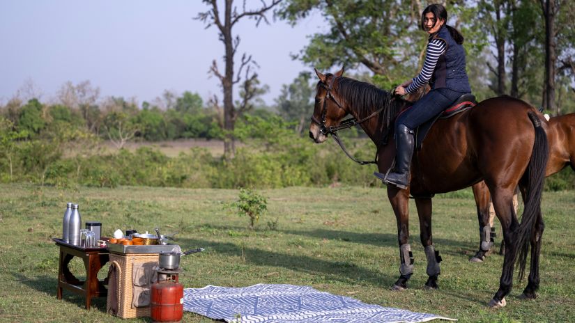 daytime shot of a woman riding a horse with a picnic setup beside her - Aalia Jungle Retreat and Spa, Bhagwanpur