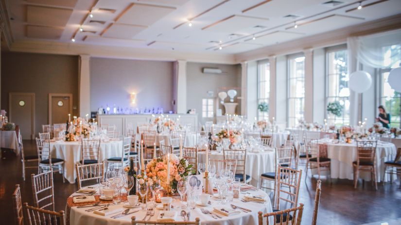 An elaborate banquet hall with round table seating and sun shining through the floor to ceiling windows