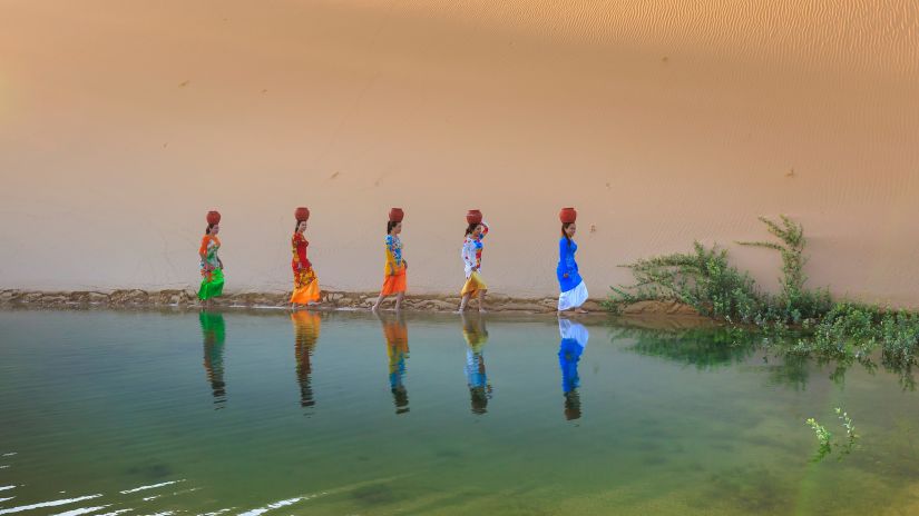 women carrying pots on their heads and walking near the lake