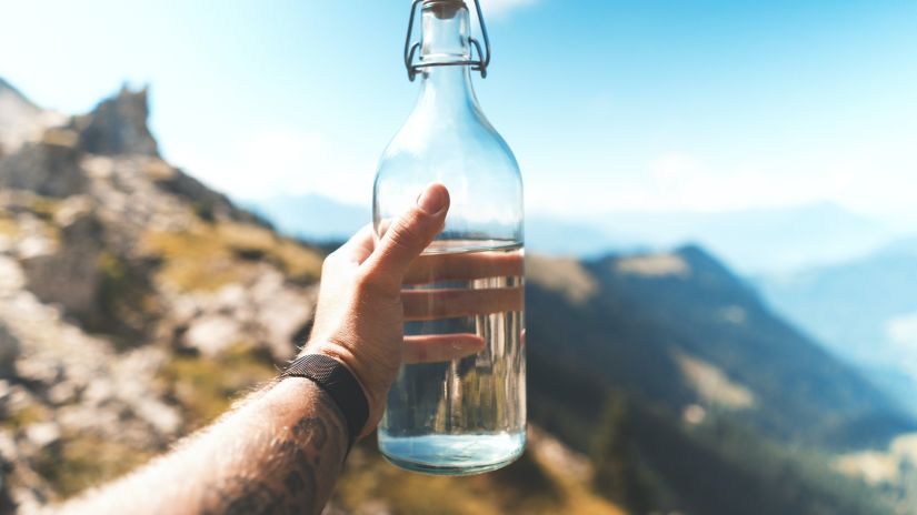 A person holding a reusable glass water bottle amidst mountains