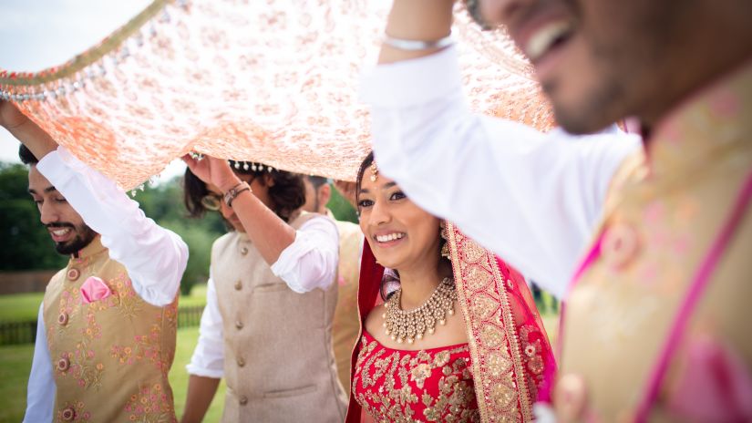 a bride walking towards the mantap with guys holding a dupatta over her