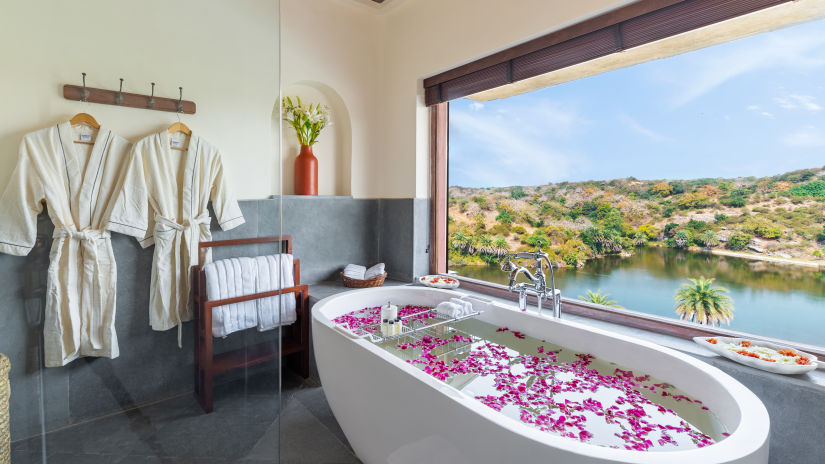 a bathtub with water and flower petals and bathrobes hung on the wall in the bathroom at one of the rooms - Chunda Shikar Oudi, Udaipur
