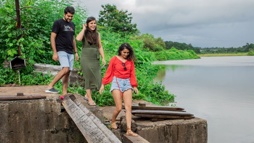 2 women and 1 man walking on a makeshift bridge with a lake on the right hand side - Heritage Village Resort & Spa, Goa