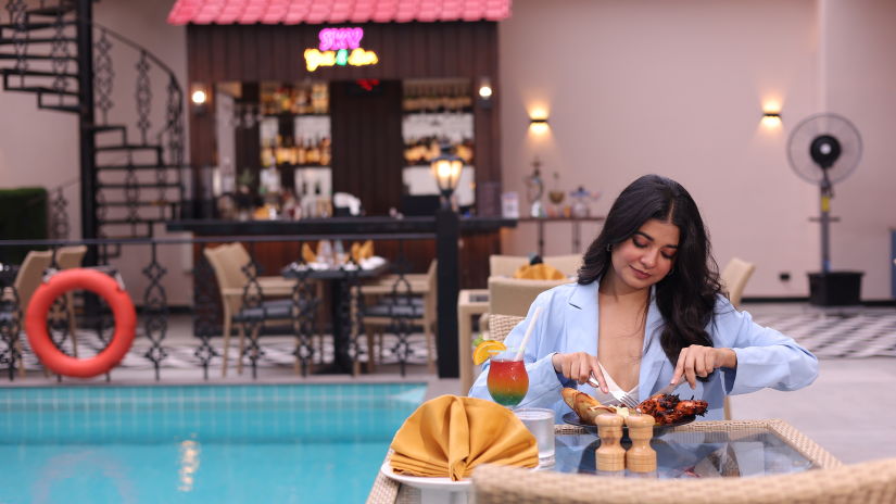 A woman feasting on food at her table next to the swimming pool at Skygrill restaurant with the bar counter in the background