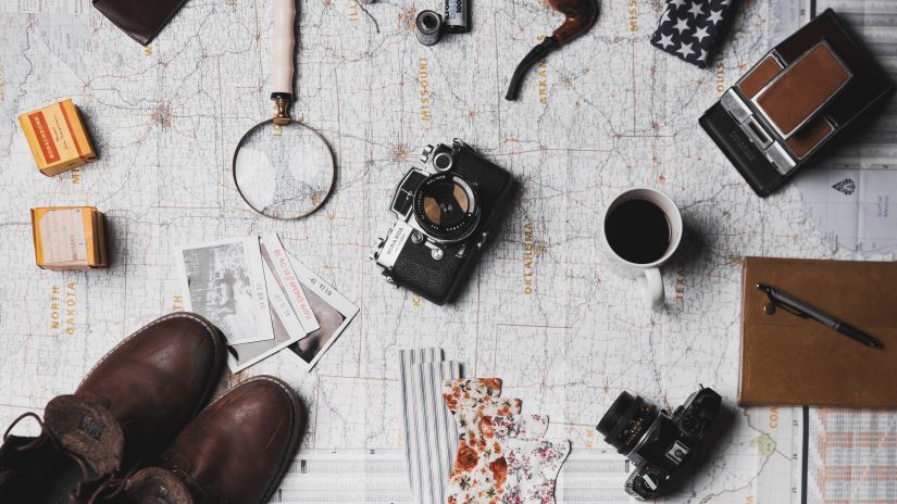 Boots, camera, coffee mug, passport, magnifying glass, a large map and other things on a table