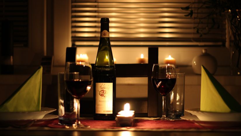 A table with candlelight, bottle of wine, wine glasses that are set up for a romantic candlelight dinner