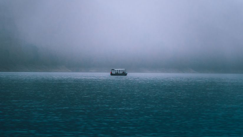 a lone boat on a river surrounded by misty mountains