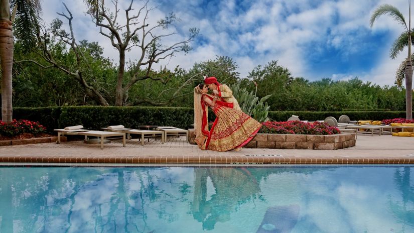 a couple standing by the pool in wedding attire for a photoshoot