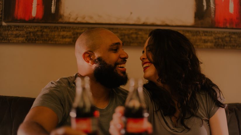 a couple looking into each other and smiling holding a bottle of cola