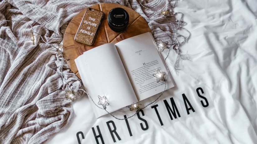 an open book with lights on it and christmas written below it and a phone and a camera lens above the book