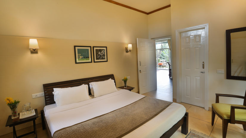 a king size premium bed with white lines with pillows and an entrance door on the right - Lamrin Norwood Green, Palampur