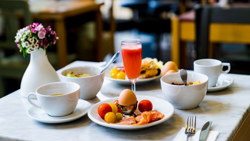 A table with breakfast items on it featuring eggs, fruits, juices and coffee