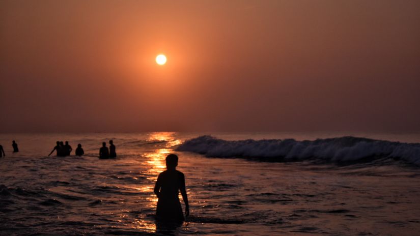 a person in the water on a beach with others in the distance during sunset